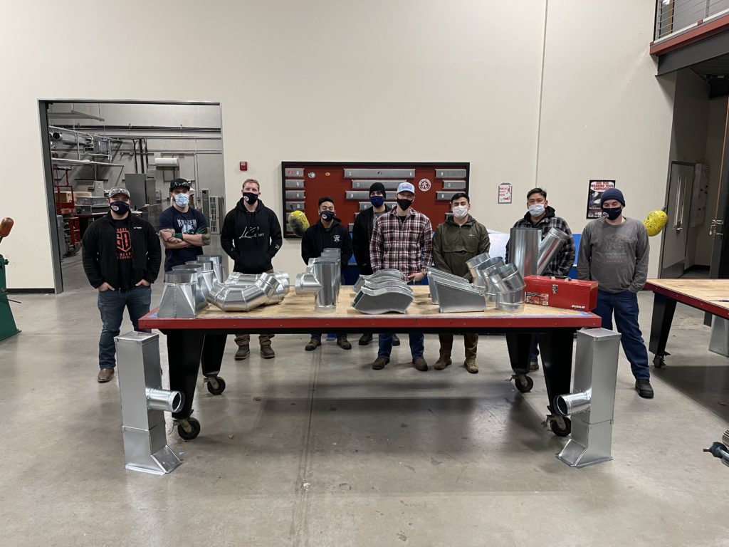 SMART Heroes graduates standing together around a table of parts.