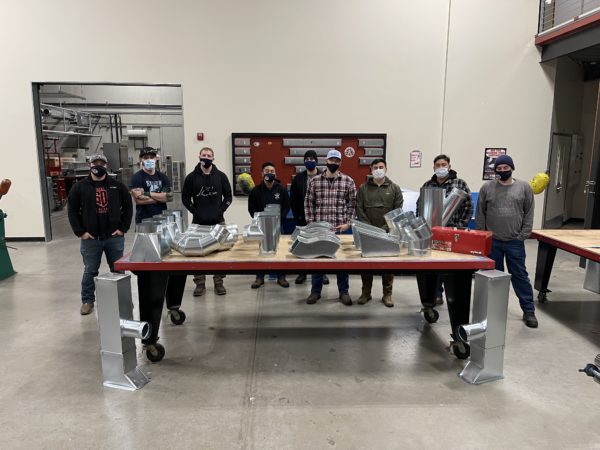 SMART Heroes graduates standing together around a table of parts.