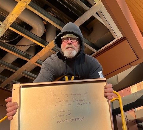 Man holding a white board with "in loving memory" written for Carrie Barber.